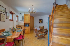 A dining area with a wooden table set for four, a chandelier, and a staircase to the right.