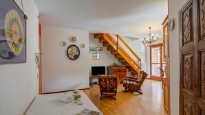 A spacious living area with a wooden staircase, a dining table with chairs, and a television. - Il Rododendro  (City Center) (Bardonecchia)