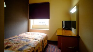 Habitación de hotel con cama, ventana con persiana oscura, escritorio pequeño y televisor, y espejo.