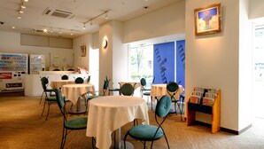 Un restaurante con mesas redondas, sillas verdes y una máquina expendedora.