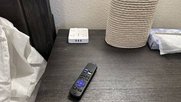 A remote control, a power strip, and a tissue box on a wooden nightstand.