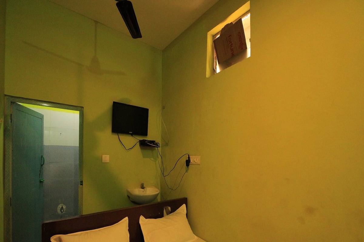 Quarto de hotel com uma cama, televisão presa à parede, pia e porta.
