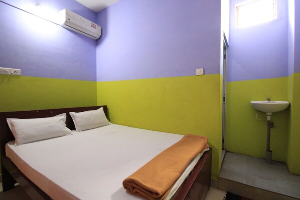 A room with a bed, a wall-mounted air conditioner, a sink, and a window.