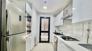 Cozinha moderna com eletrodomésticos de aço inoxidável, armários brancos e uma ilha central.