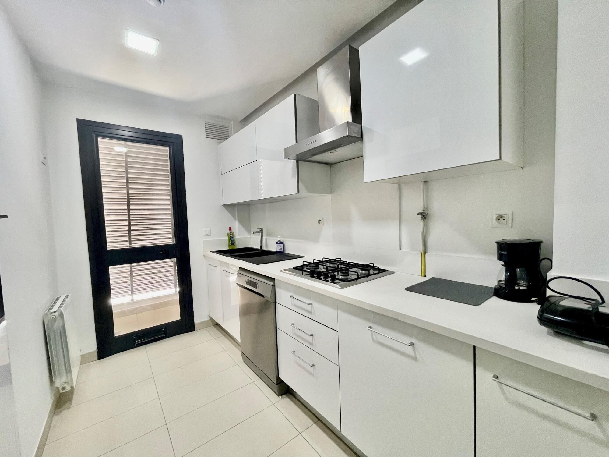A modern kitchen with white cabinets, a gas stove, a dishwasher, and a coffee maker.