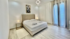 Quarto moderno com cama grande, mesas de cabeceira, luminária no teto, um quadro e janela com cortinas.