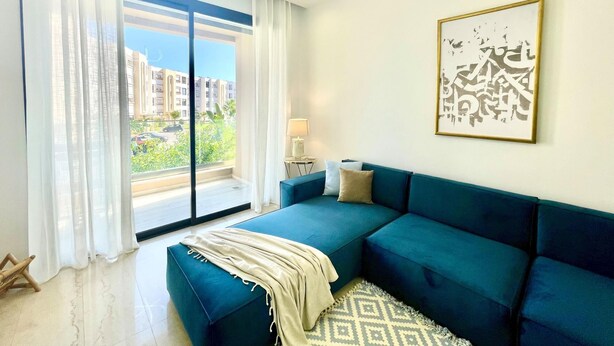 Sala de estar moderna com sofá azul, tapete estampado e vista para a cidade através de grandes janelas.