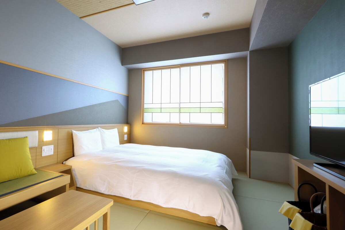 A hotel room with a bed, a sofa, a television, and a window.