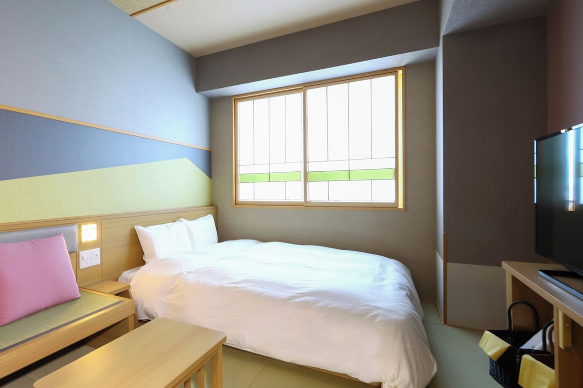 A hotel room with a bed, a small table, a bench, a TV, and a window.