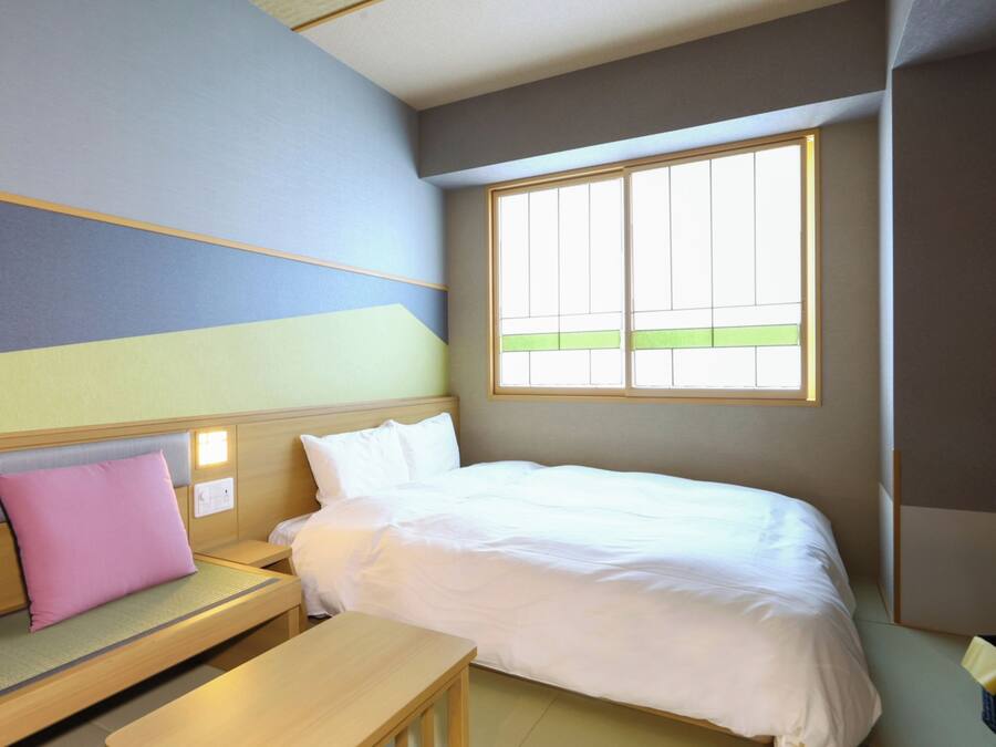 A hotel room with a bed, a small table, a bench, a TV, and a window.