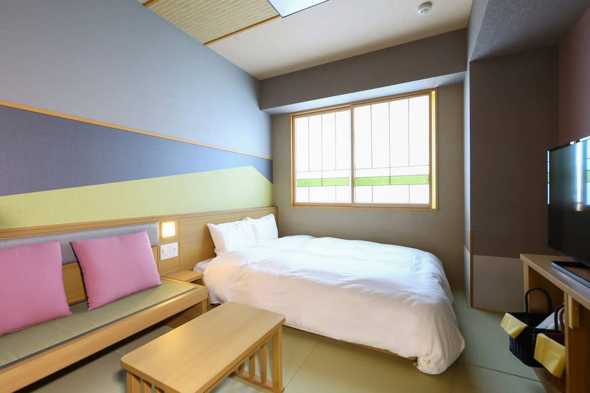 A hotel room with a bed, a sofa with cushions, a wooden table, and a TV on a stand.