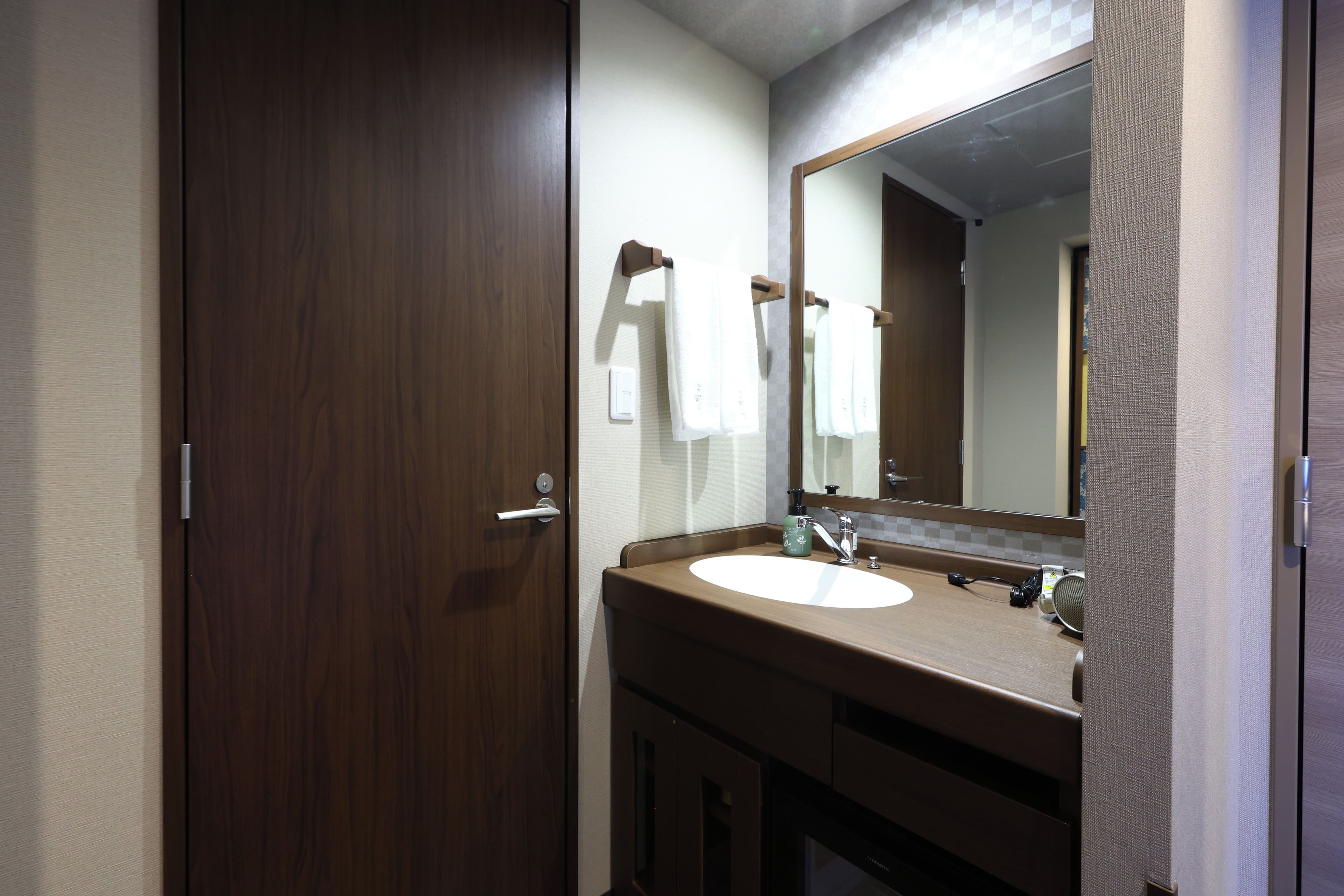 Un baño con puerta de madera, un lavabo con espejo y un perchero para toallas.