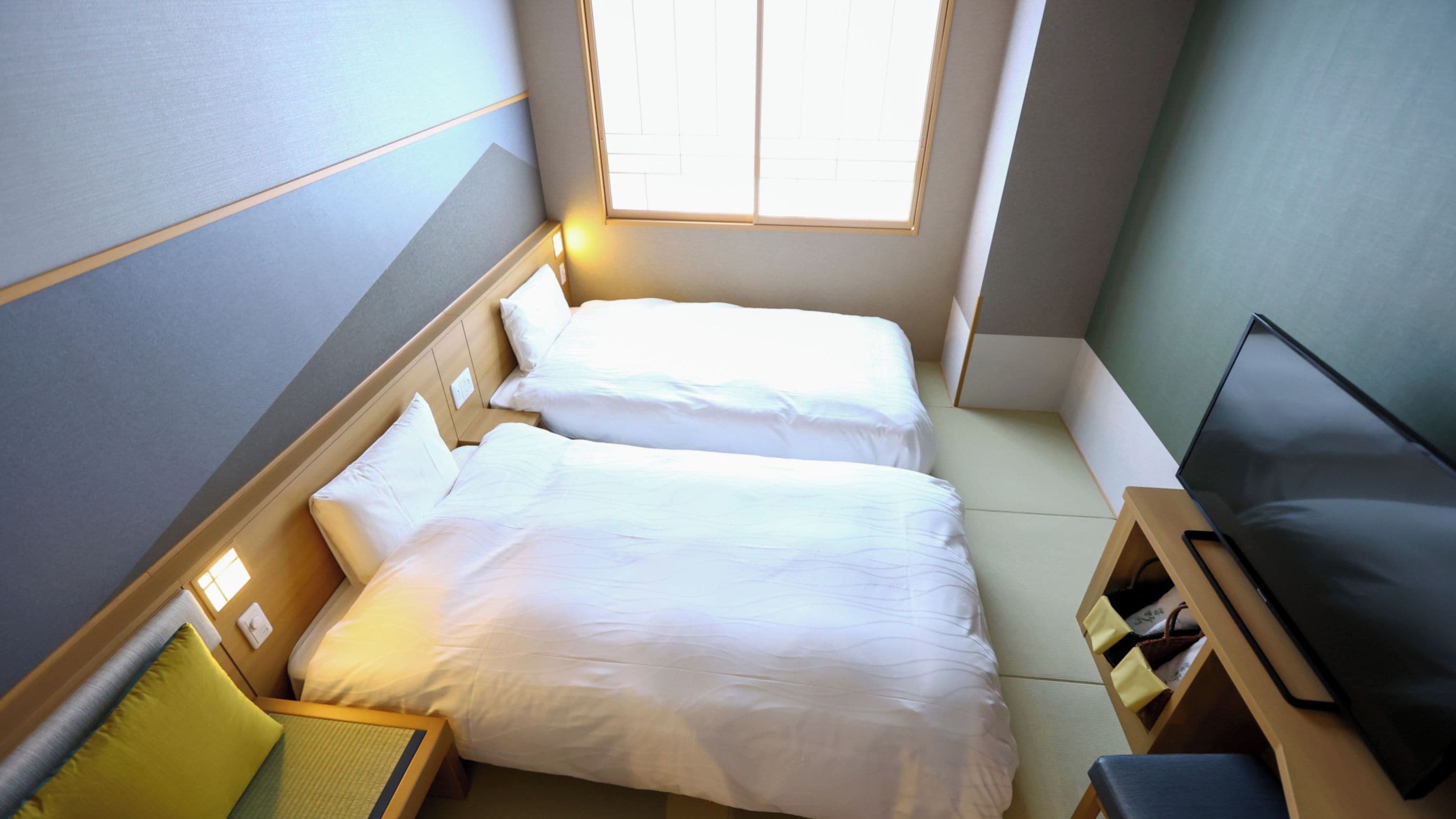 A compact hotel room with two beds, a small seating area, and a television.