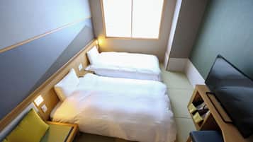 A compact hotel room with two beds, a small seating area, and a television.