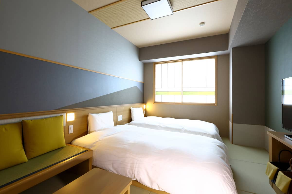 A hotel room with a large bed, a sofa, a TV, and a window providing natural light.