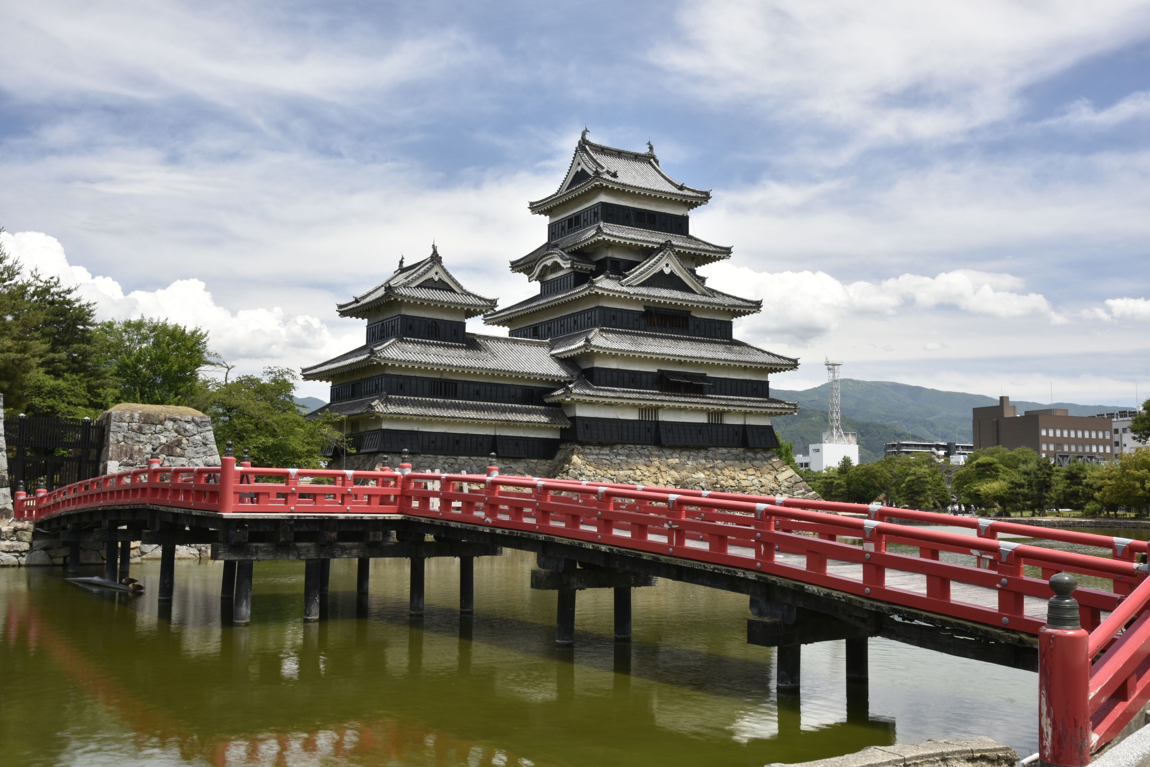 Een traditioneel Japans kasteel met meerdere verdiepingen en een rode brug die ernaar leidt.