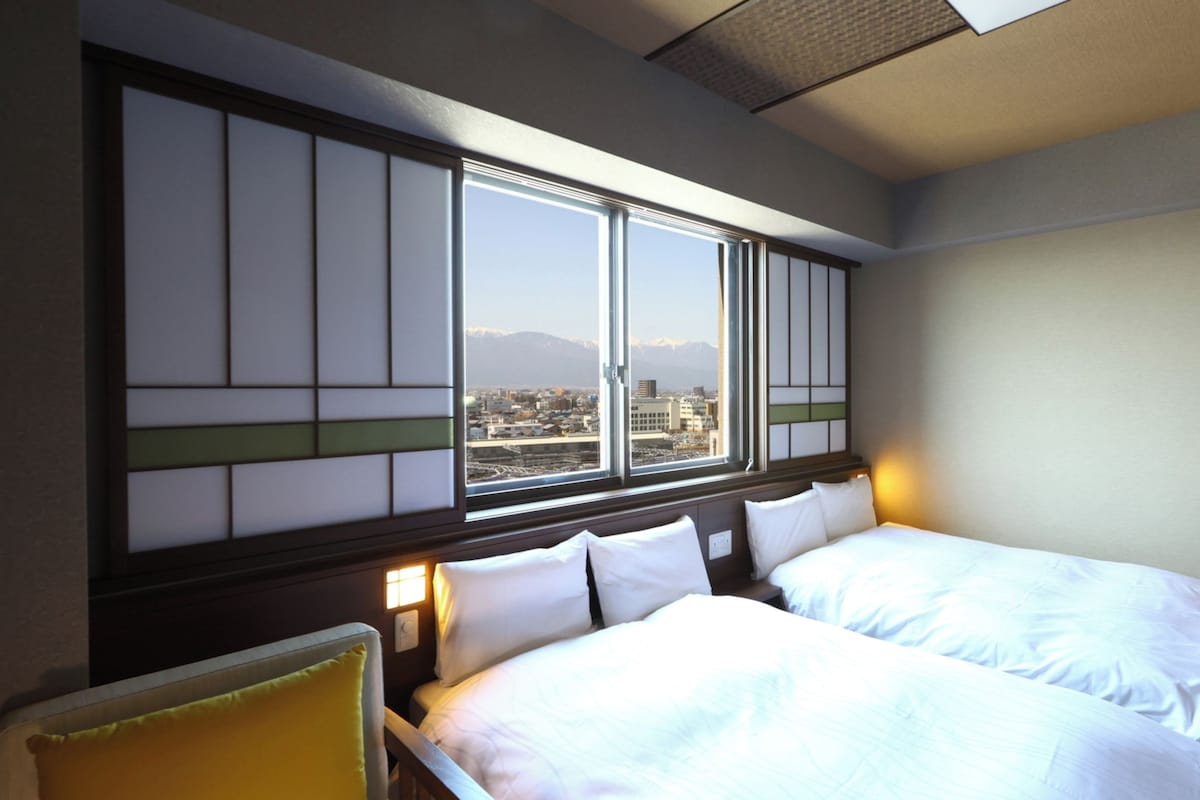 A hotel room with two beds, a view of a cityscape through large windows, and a traditional-style wall panel.