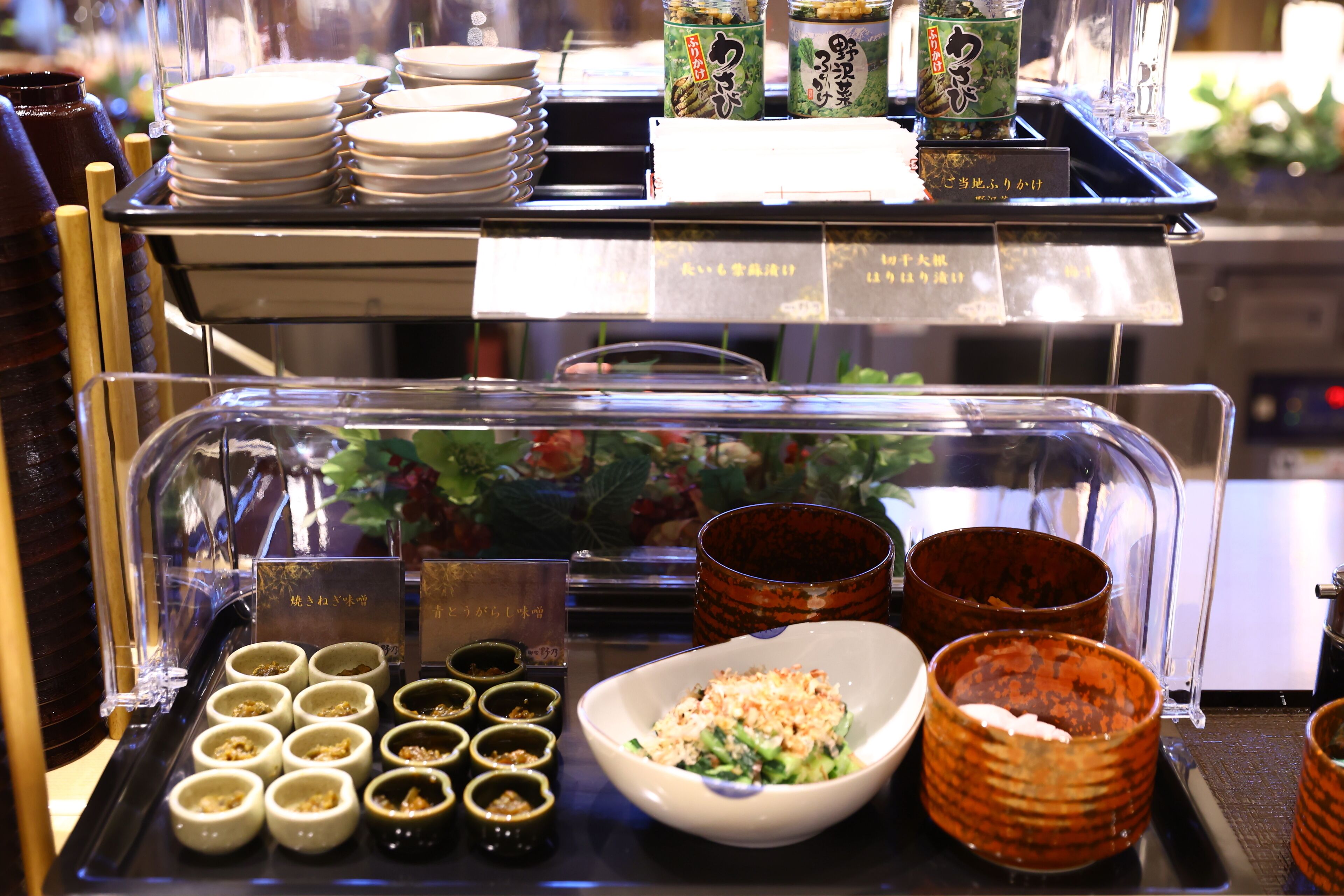 Una presentación de comida con diversos platos y condimentos, incluyendo recipientes pequeños y un bol grande de ensalada.