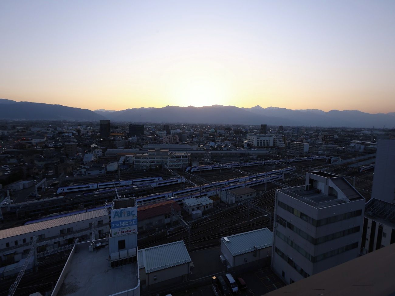 A cityscape at dusk with mountains in the background, buildings, and a train station.