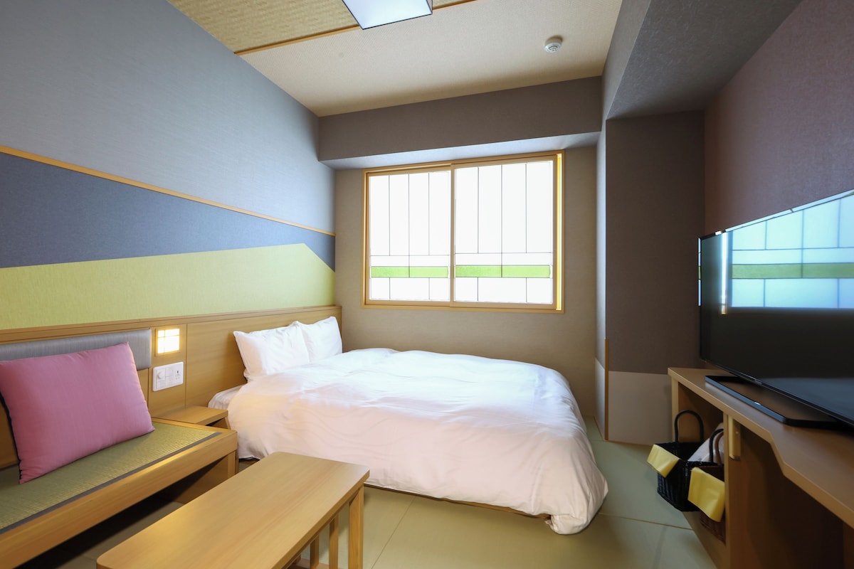 A hotel room with a bed, a television, a bench, and a window.