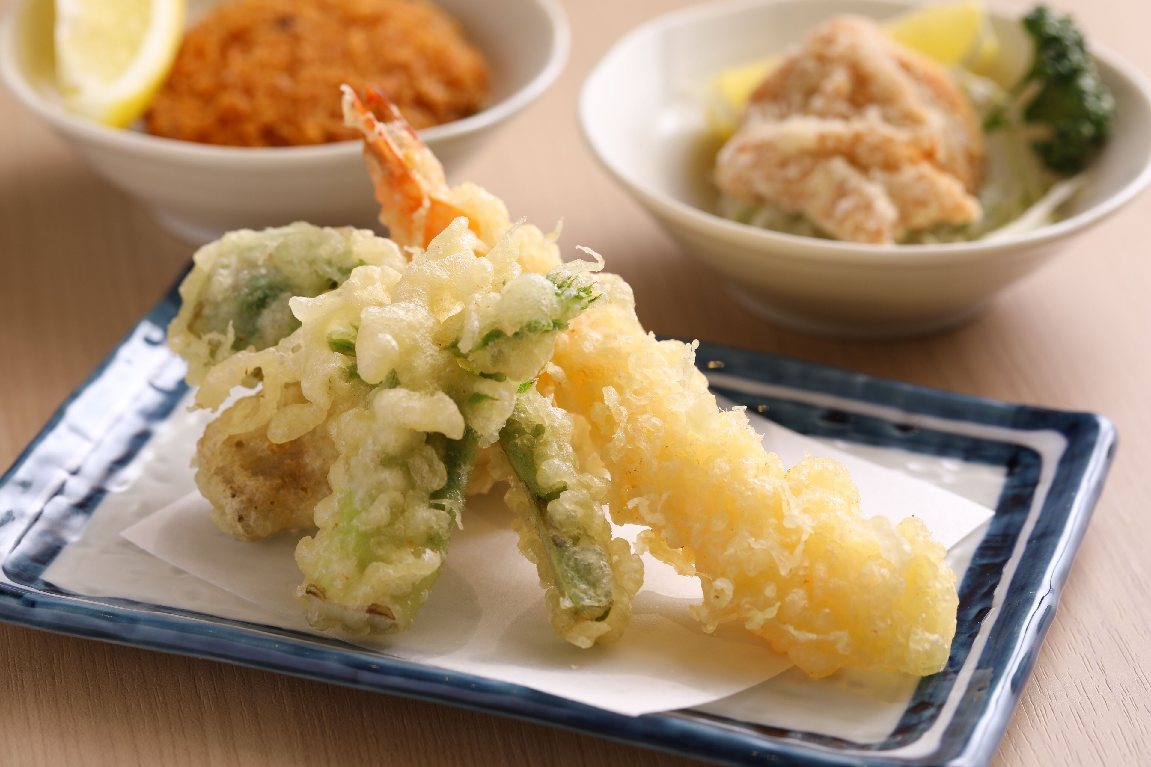 A plate of tempura with shrimp and vegetables, accompanied by a bowl of miso soup and another dish with fish and greens.