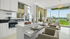 Cozinha moderna com ilha central, armários brancos e vista para a cidade por grandes janelas.