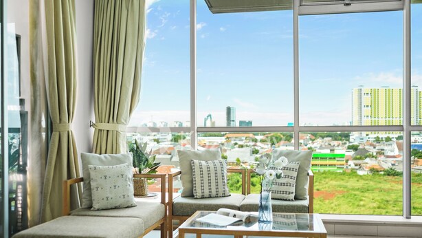 Uma sala de estar moderna com um conjunto de sofás, uma mesa de centro de vidro e vista para a paisagem urbana através de janelas amplas.