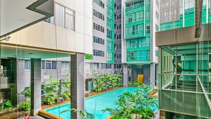 Um edifício moderno com piscina no terraço, rodeado por vegetação e um elevador de vidro.