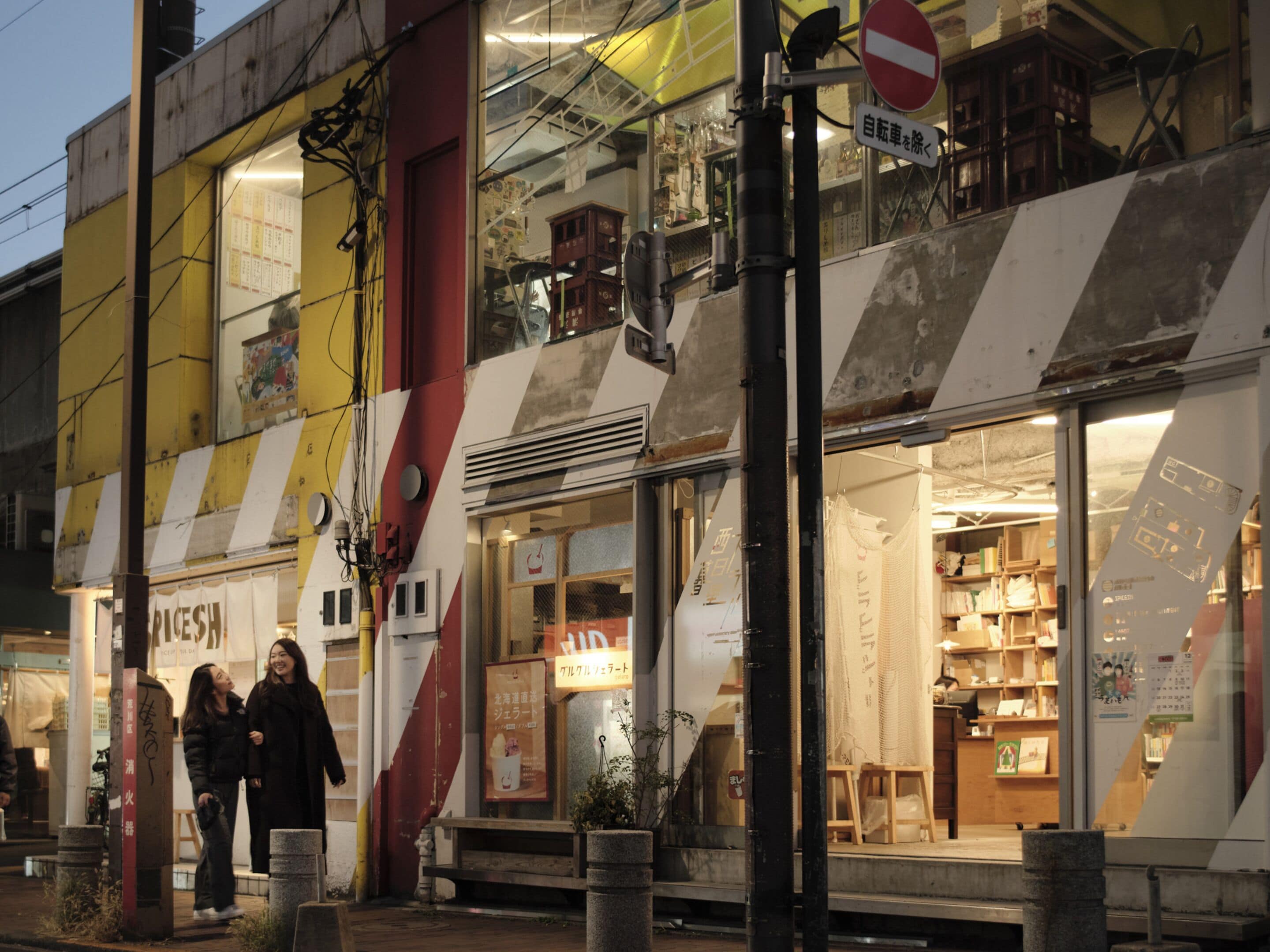 A building with a storefront featuring a sign in a foreign language, a staircase leading to an upper level, and a street with pedestrians.