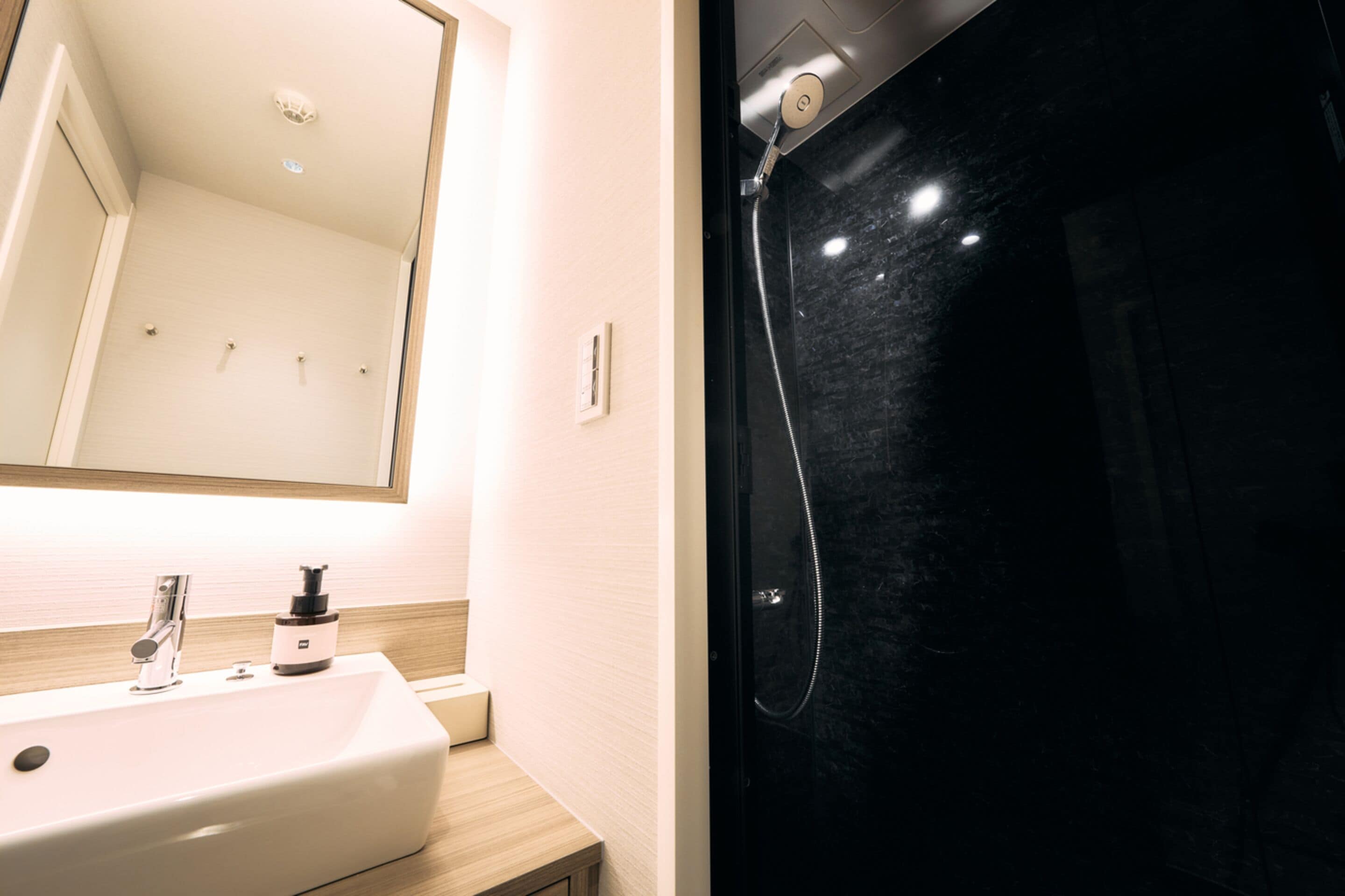 Un baño con un lavamanos blanco, un espejo y un box de ducha negro.