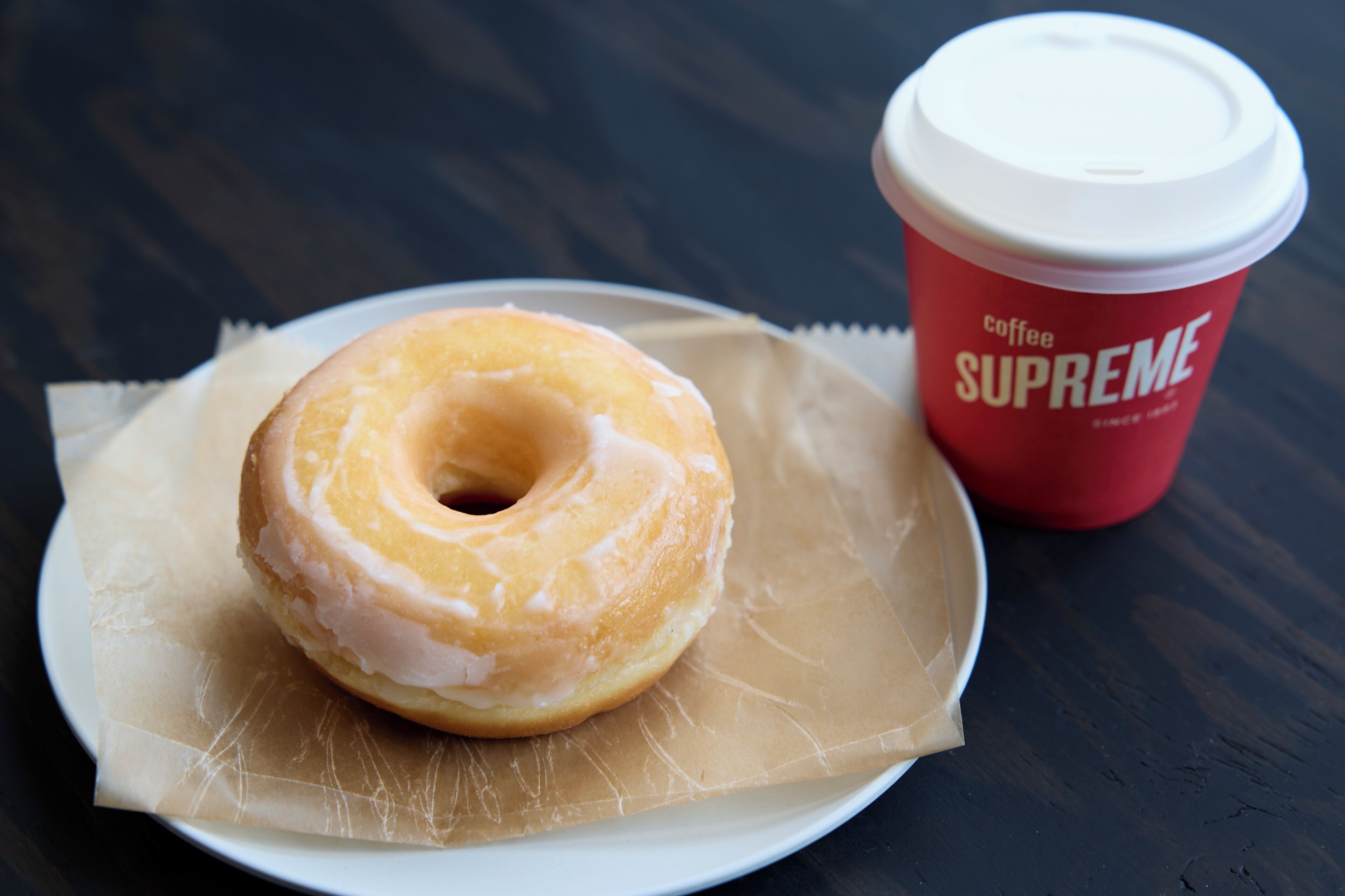A glazed donut on a plate with a red coffee cup labeled "Coffee Supreme" beside it.