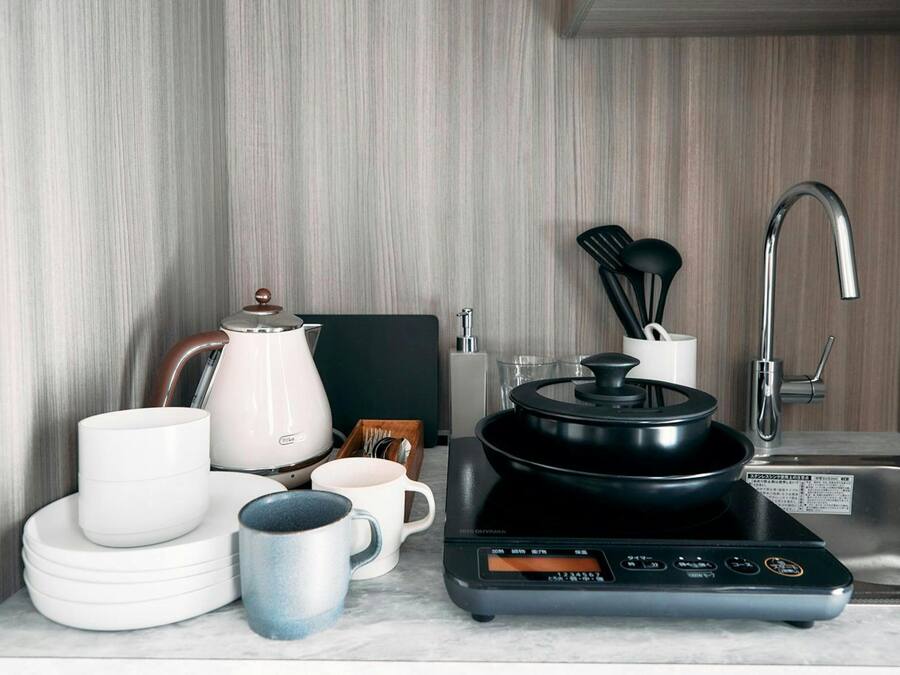 A kitchen with a modern stove, sink, and various kitchenware including plates, cups, and a kettle.