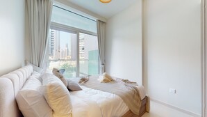 Una camera da letto con un'ampia finestra, un letto con biancheria bianca e vista su alti edifici.