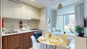 Una cucina moderna con piano cottura a gas, macchina del caffè e estintore. C'è un'area pranzo con un tavolo apparecchiato per due e un'ampia finestra con vista sulla città.