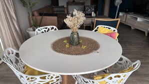 Una mesa de comedor redonda con un posavasos tejido, rodeada de sillas blancas con cojines amarillos.