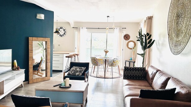 Una sala moderna con sofá, mesa de centro y sillas. Hay un comedor con una mesa y sillas. La habitación tiene un espejo grande, un reloj y adornos en las paredes.