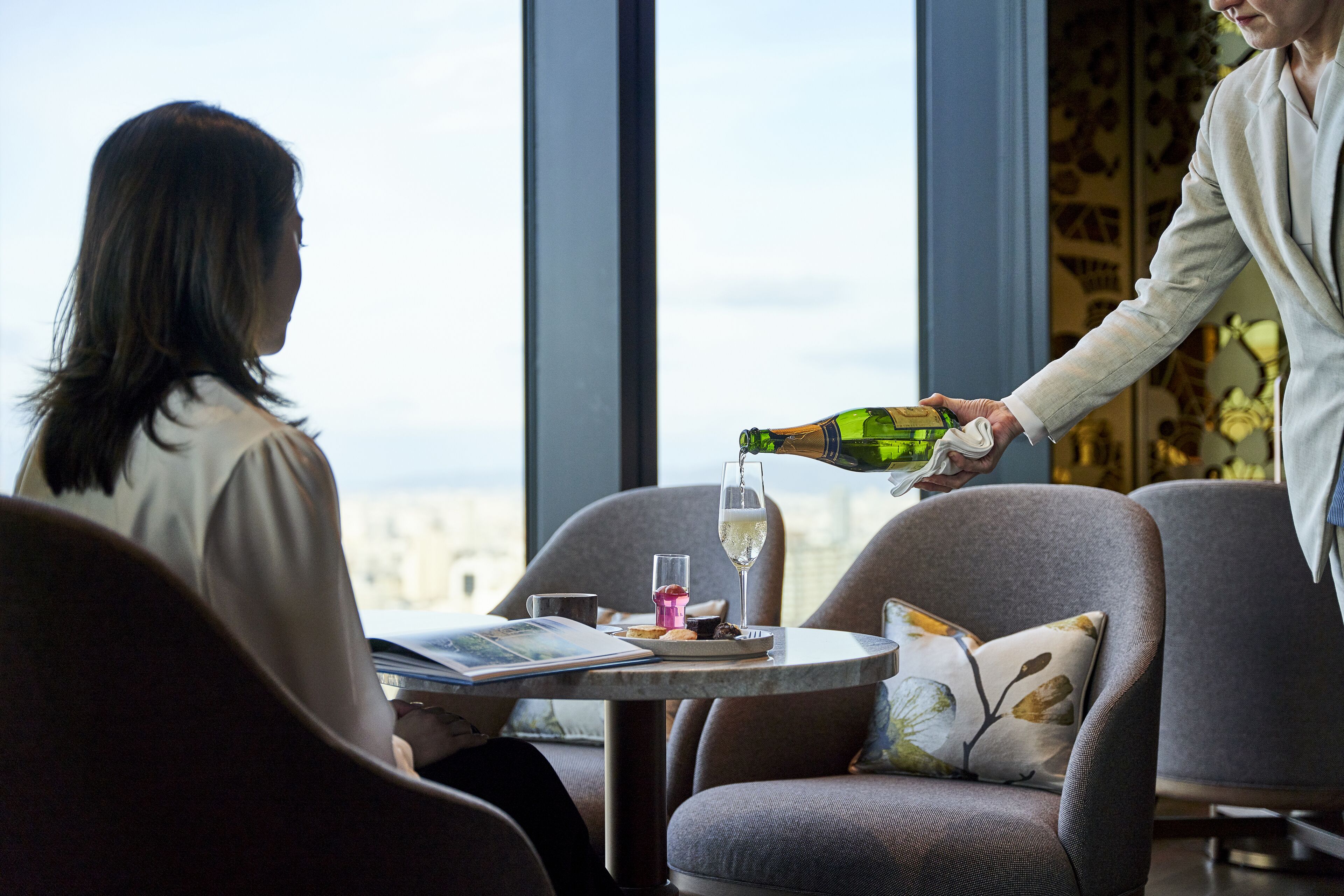 A person pouring a drink into a glass at a table with a view of the city.