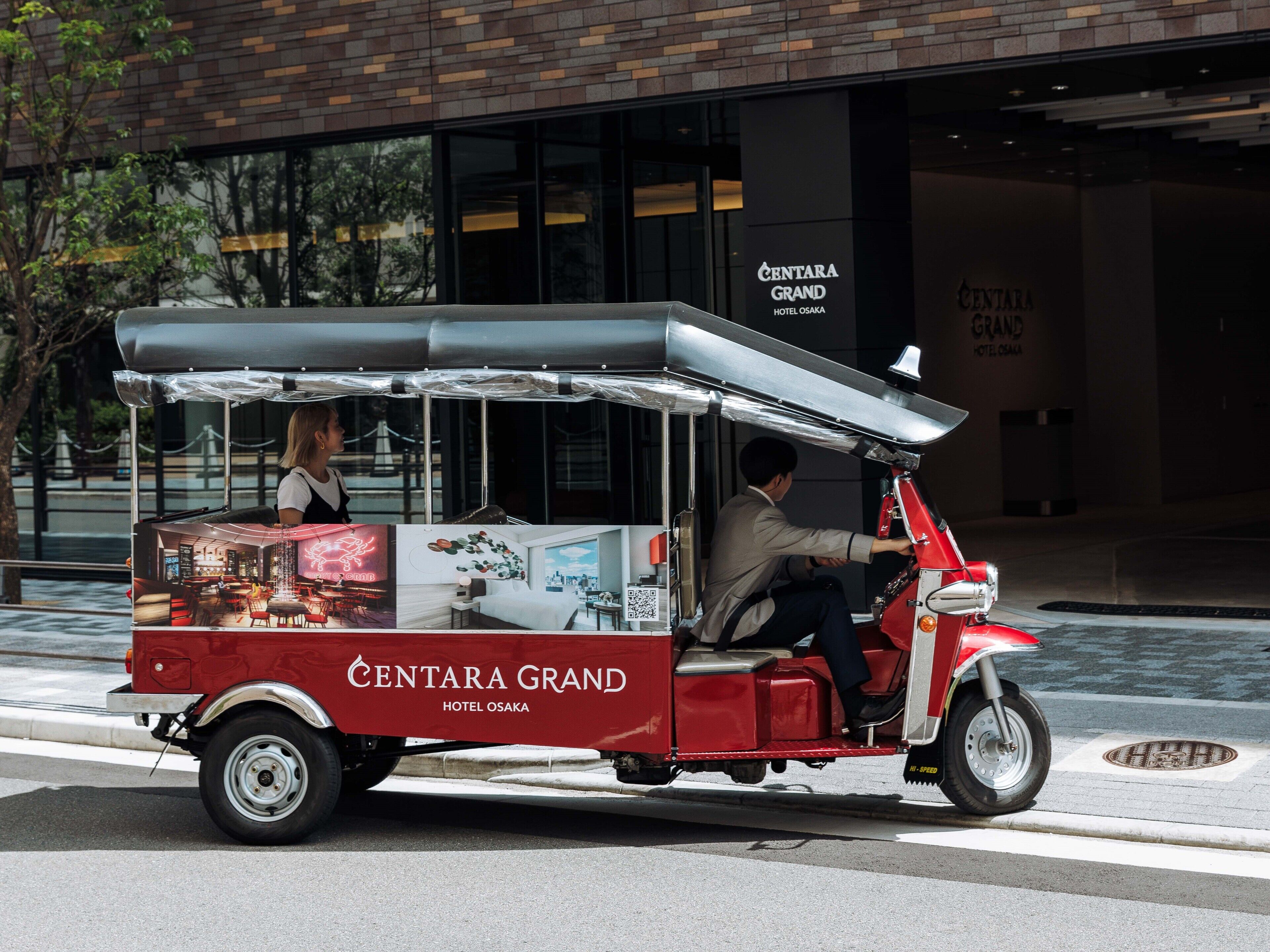 A red Centara Grand Hotel Osaka food cart with a driver and a passenger.