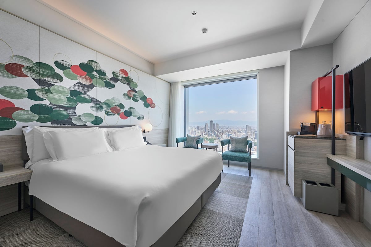 A modern hotel room with a large bed, a city view, a desk, and a TV.