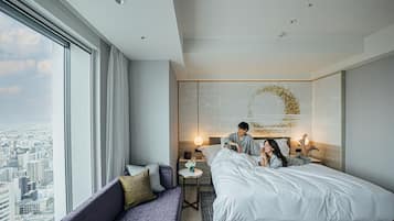 A modern hotel room with a large bed, a sofa, a small table, and a view of the city.