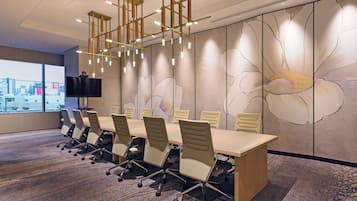 Une salle de conférence avec une longue table, des chaises, un téléviseur et une fresque murale représentant des motifs floraux.