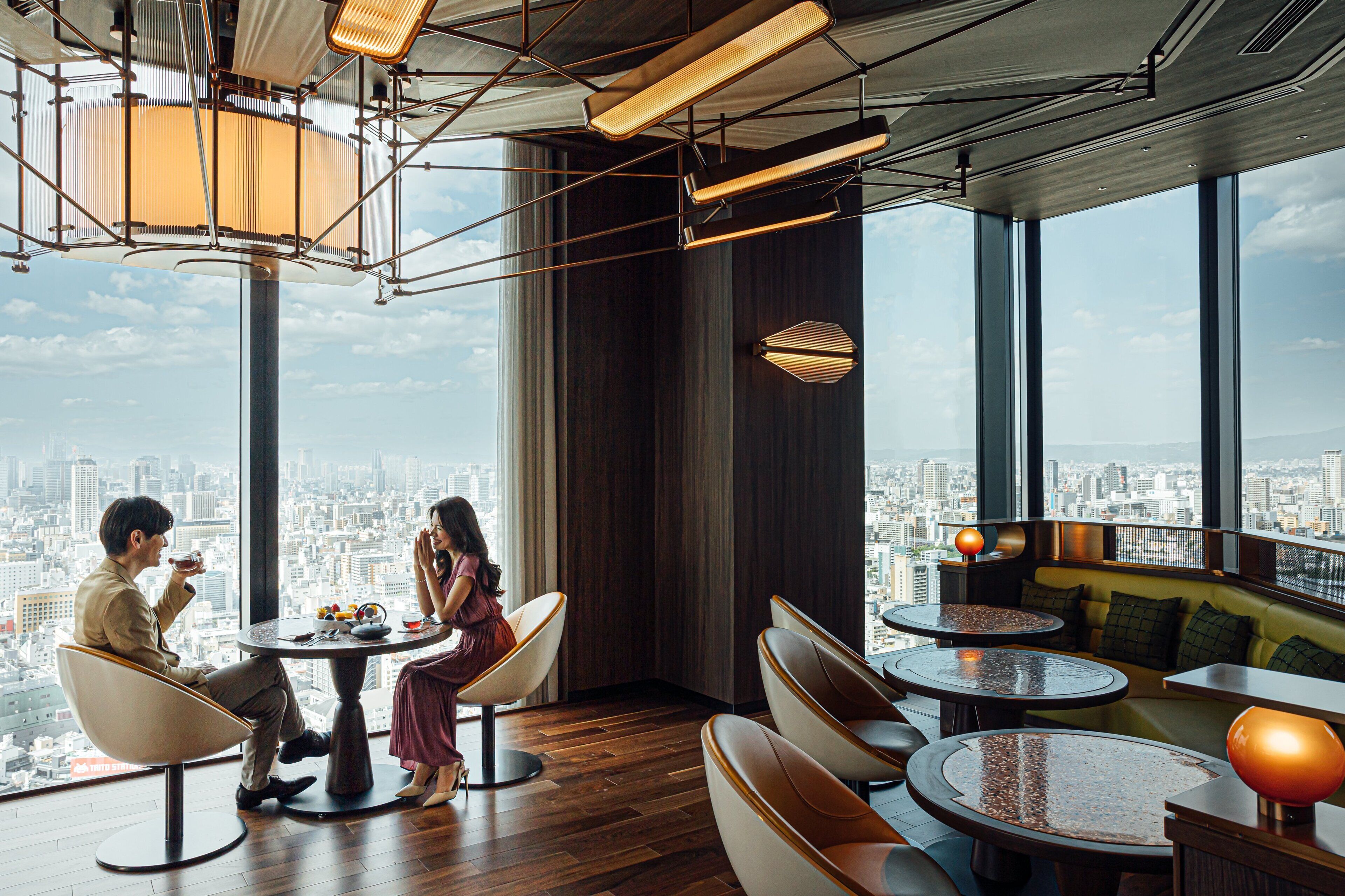 A modern interior with a city view, featuring round tables, comfortable seating, and contemporary lighting.