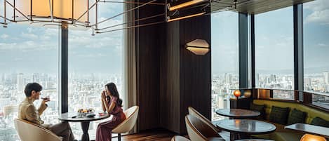 Un interior moderno con vistas a la ciudad, que presenta mesas redondas, asientos cómodos e iluminación contemporánea.