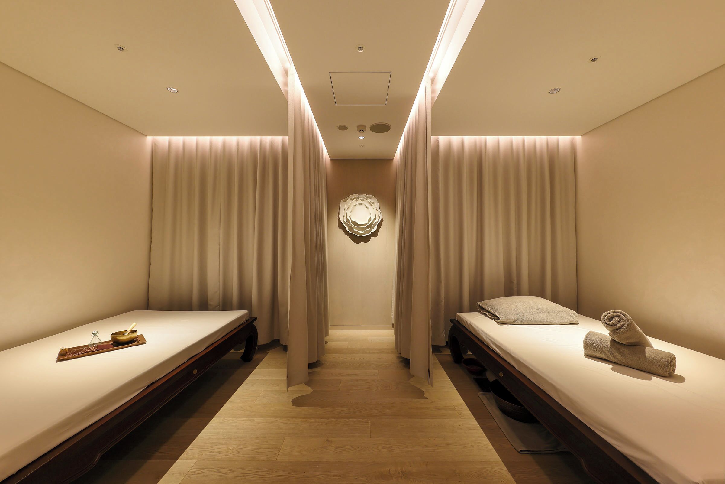 A hotel room with two single beds, a wooden floor, and a central wall decoration.