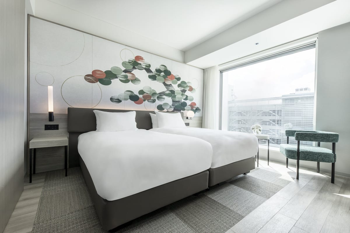 A modern bedroom with a large bed, a side table, a chair, and a city view through the window.