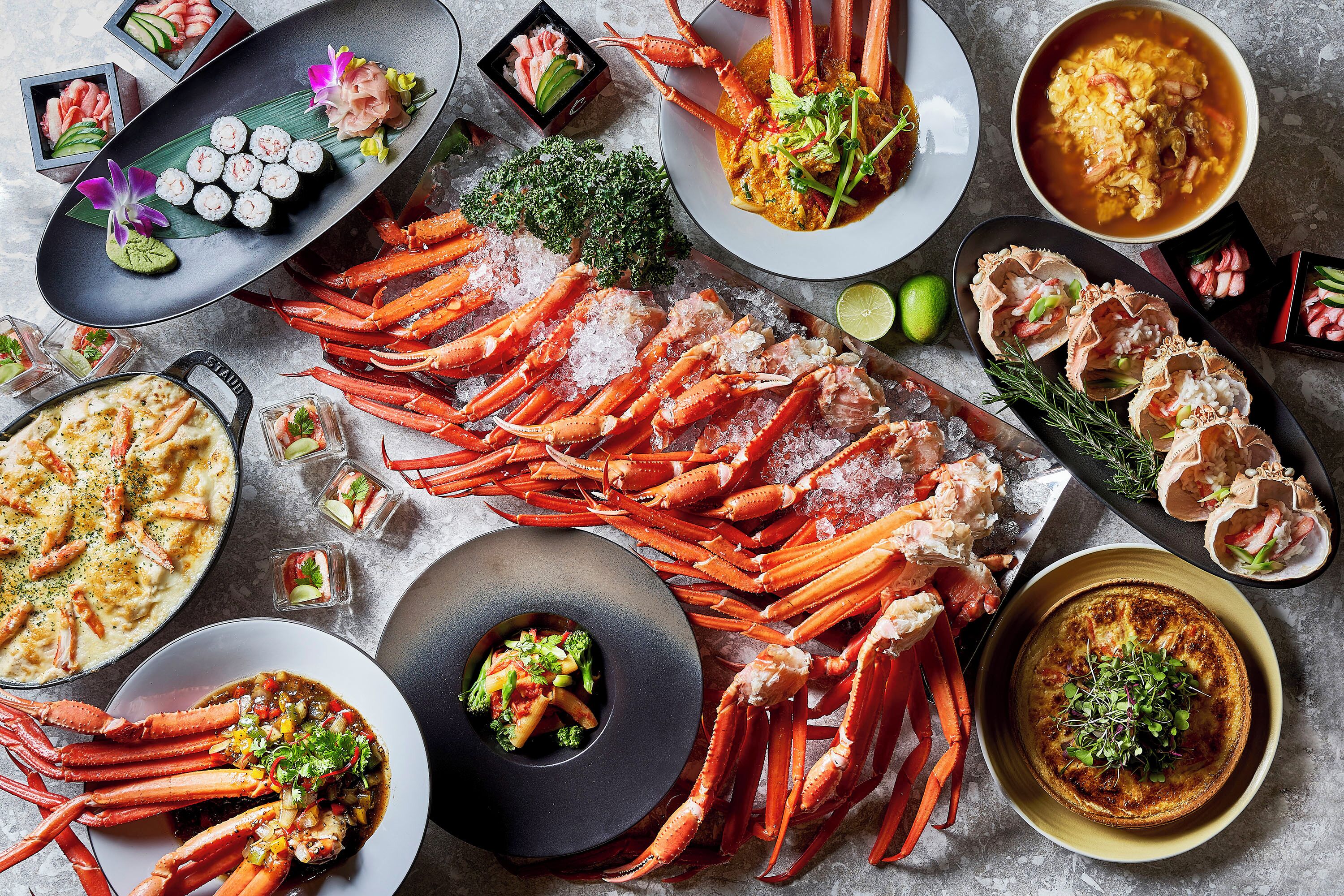 A seafood spread with various dishes including crab legs, sushi, and a bowl of soup.