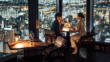 A couple dining at a table with a city view, in a modern interior with plaid chairs and a small candle on the table.
