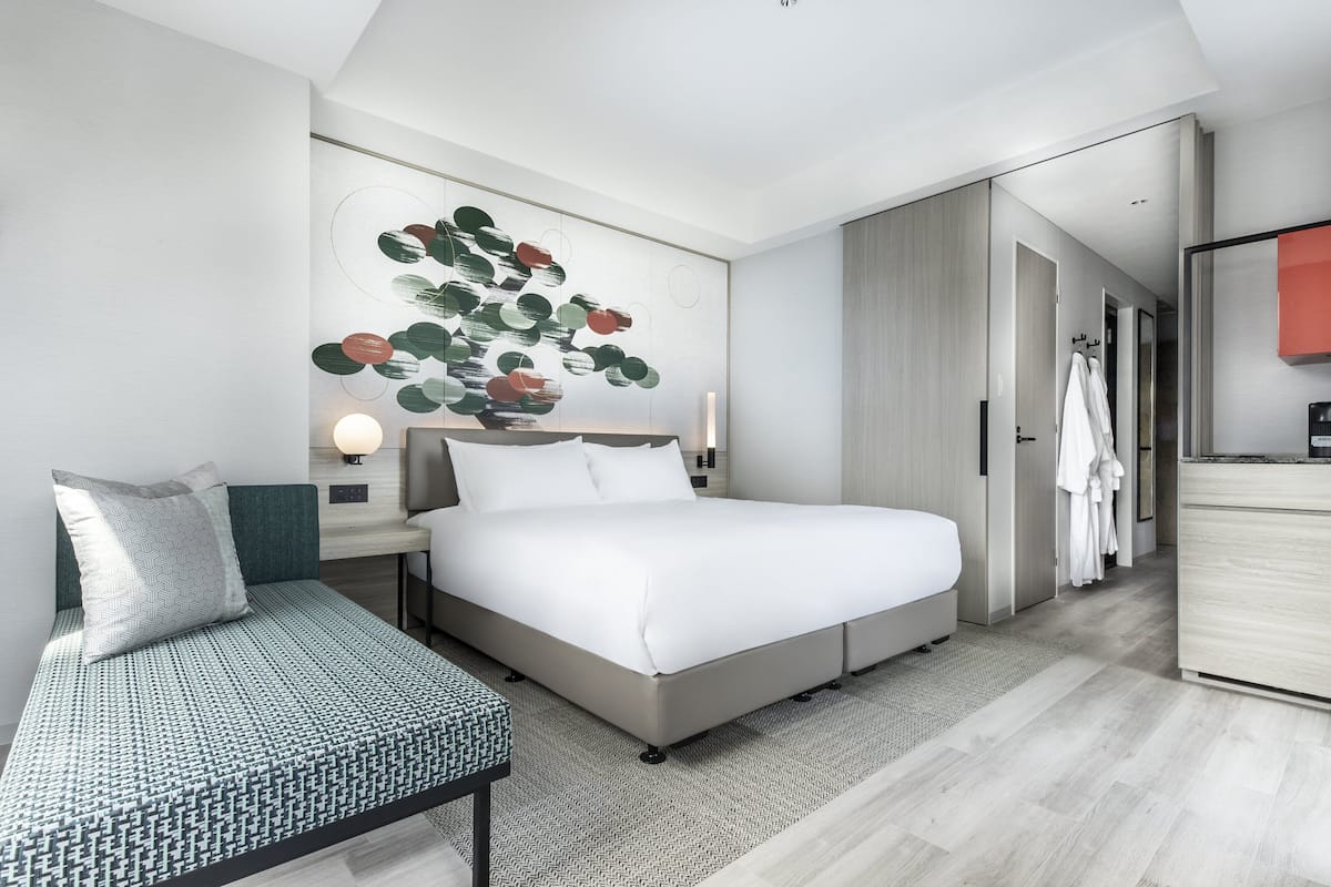 A modern hotel room with a large bed, a seating area, a desk, and a wardrobe.