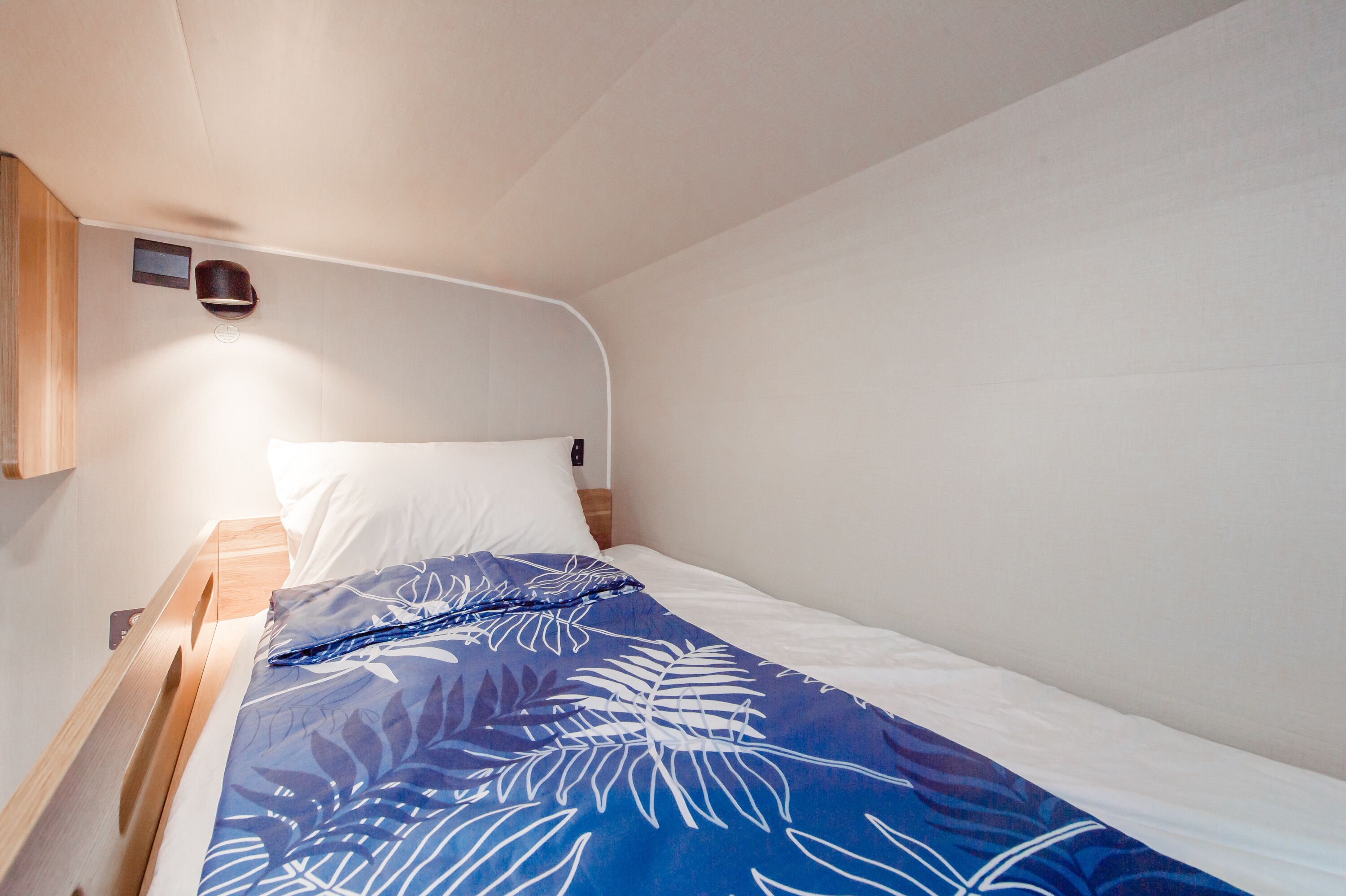 Una cama individual con una colcha azul estampada con flores, una almohada blanca y un cabecero de madera.