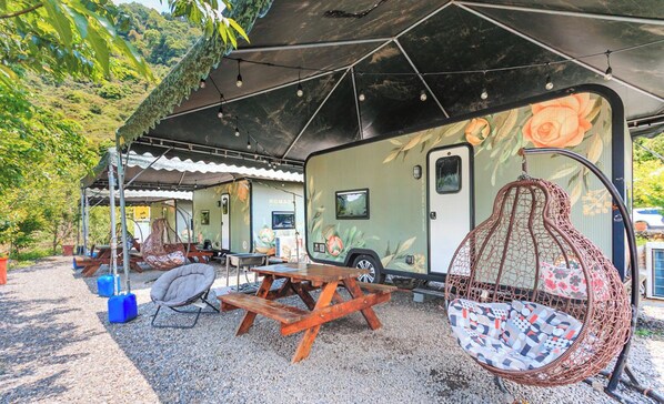 A recreational vehicle with a covered picnic area, a hanging chair, and a table.